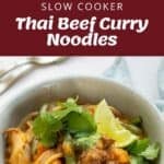 A bowl of Thai beef curry noodles with vegetables, garnished with cilantro and lime, shown with uncooked ingredients and a slow cooker.