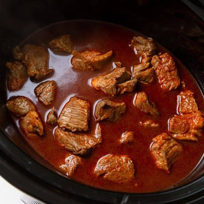 Slow Cooker Thai Beef Curry Chunks of beef simmering in a rich, red sauce inside a slow cooker.
