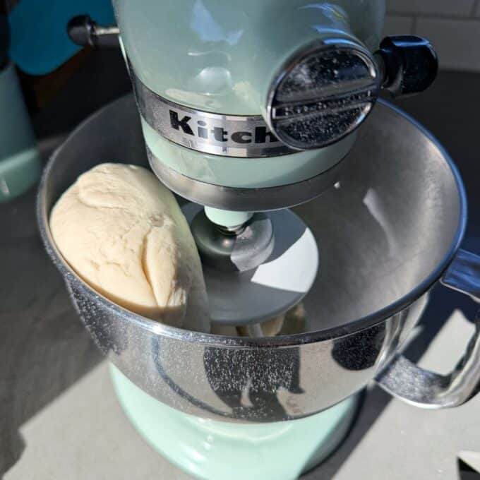 White Sandwich Bread A stand mixer with a dough hook attachment is kneading a ball of dough in a stainless steel mixing bowl.