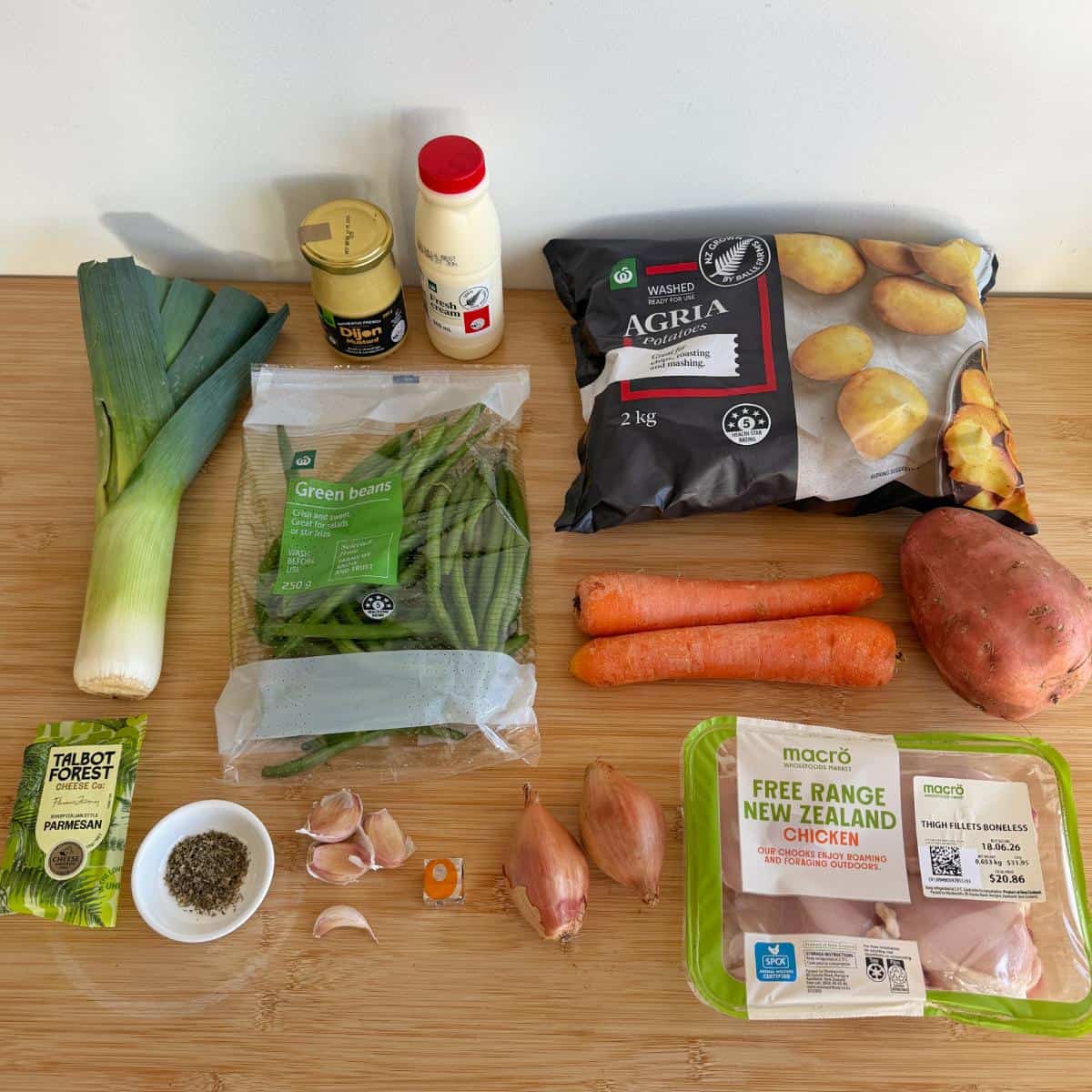 Creamy French Mustard Chicken Assorted fresh vegetables, a pack of chicken breasts, green beans, condiments, packaged potatoes, parmesan, and herbs arranged on a wooden surface.