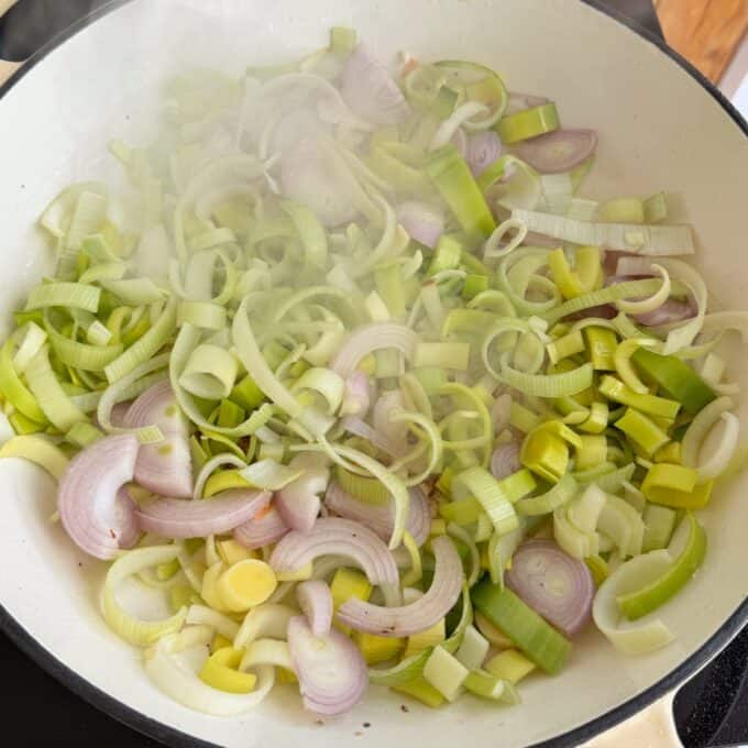 Creamy French Mustard Chicken Sliced leeks and onions are sautéing in a white pan, with visible steam rising from the vegetables.