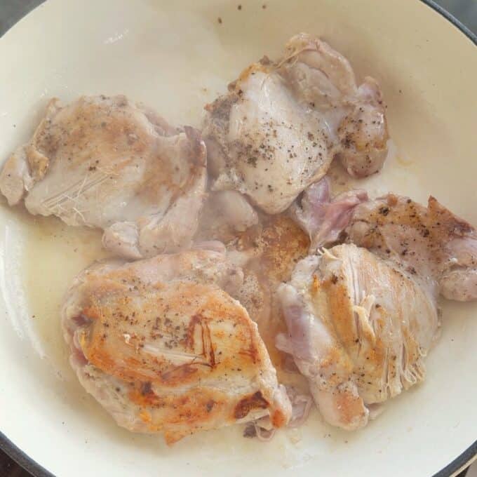 Creamy French Mustard Chicken Four pieces of chicken are searing in a skillet, lightly browned and seasoned with pepper, with some visible oil and steam rising.