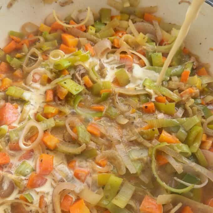 Creamy French Mustard Chicken Chopped carrots, leeks, and onions simmer in a pot as cream is being poured in, creating a hearty vegetable soup.