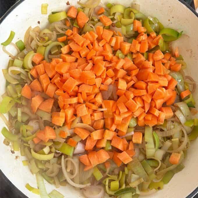 Creamy French Mustard Chicken Diced carrots, sliced leeks, and onions are being sautéed together in a large white pan.