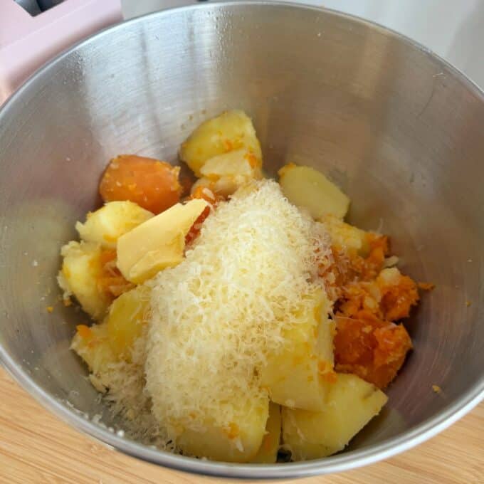 Creamy French Mustard Chicken Boiled potatoes and carrots, topped with a pat of butter and grated cheese, are placed in a metal mixing bowl on a wooden surface.