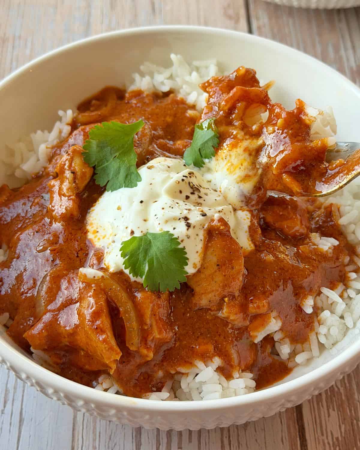 A bowl of chicken curry over white rice, topped with a dollop of sour cream and fresh cilantro leaves.