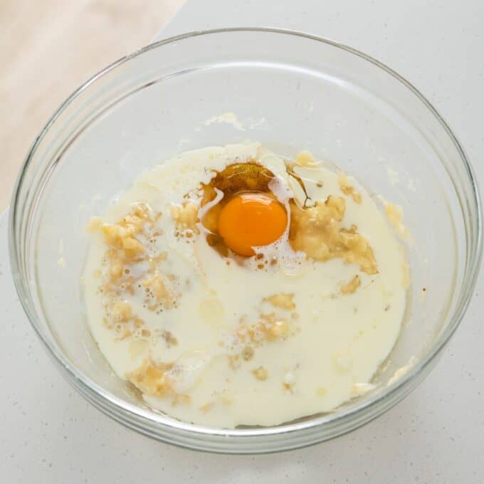 Banana Cinnamon Crumble Muffins A raw egg, mashed banana, and milk in a glass mixing bowl.