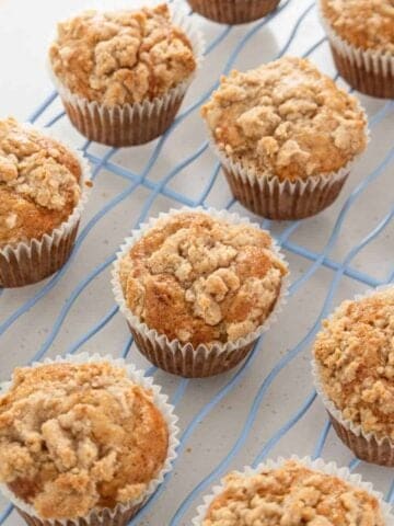 A grid of crumb-topped muffins cooling on a wire rack.