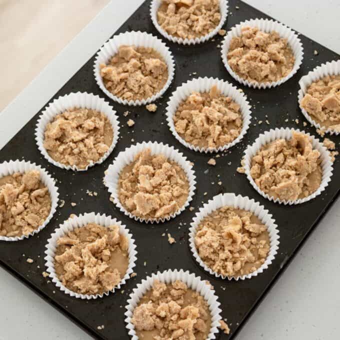 Banana Cinnamon Crumble Muffins A muffin tin filled with twelve paper-lined muffin cups containing batter topped with streusel.