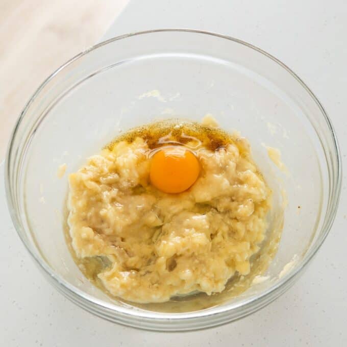 Banana Cinnamon Crumble Muffins A raw egg cracked into a bowl of mashed bananas.