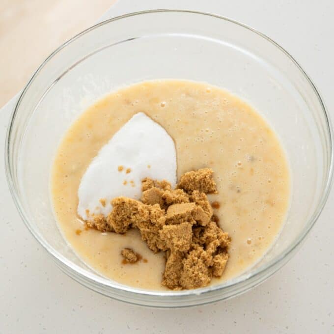 Banana Cinnamon Crumble Muffins A glass mixing bowl containing batter with a mound of white sugar and a pile of brown sugar on top.
