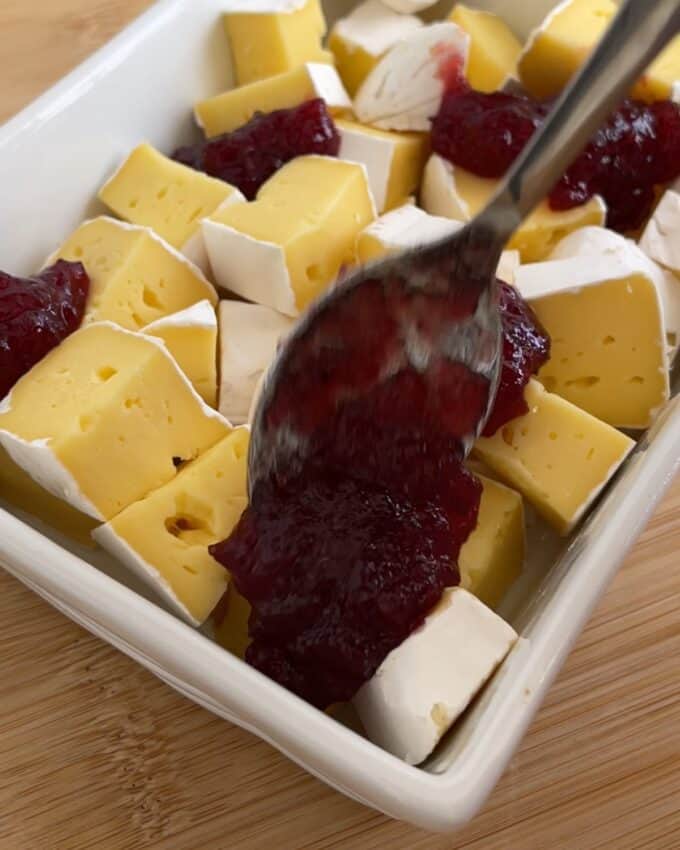 Air Fryer Cranberry Brie Dip A spoon spreads cranberry sauce over cubes of Brie cheese in a baking dish.