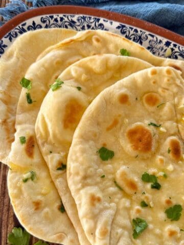 Stack of garlic naan bread garnished with fresh parsley on a patterned plate.