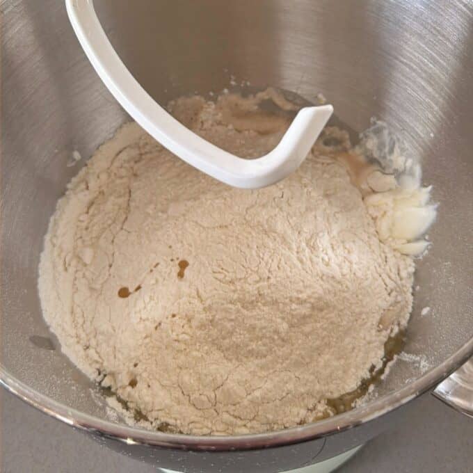 Homemade Garlic Naan A stand mixer bowl containing flour, liquid, and a dollop of butter with a dough hook attachment positioned above.