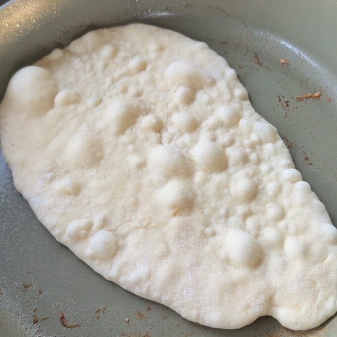 Homemade Garlic Naan A piece of flatbread with bubbles cooking in a frying pan.
