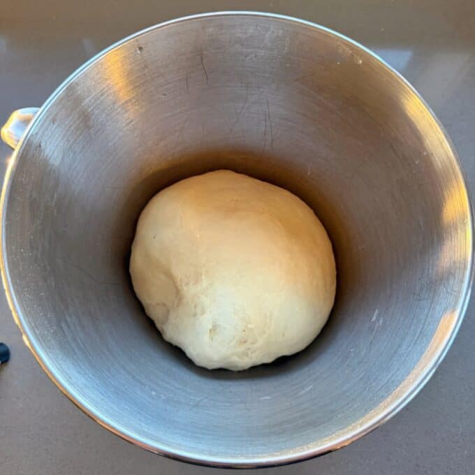 Homemade Garlic Naan A ball of raw dough resting in a stainless steel mixing bowl.