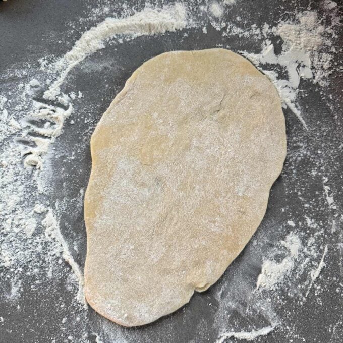 Homemade Garlic Naan A piece of rolled-out dough on a flour-dusted surface.