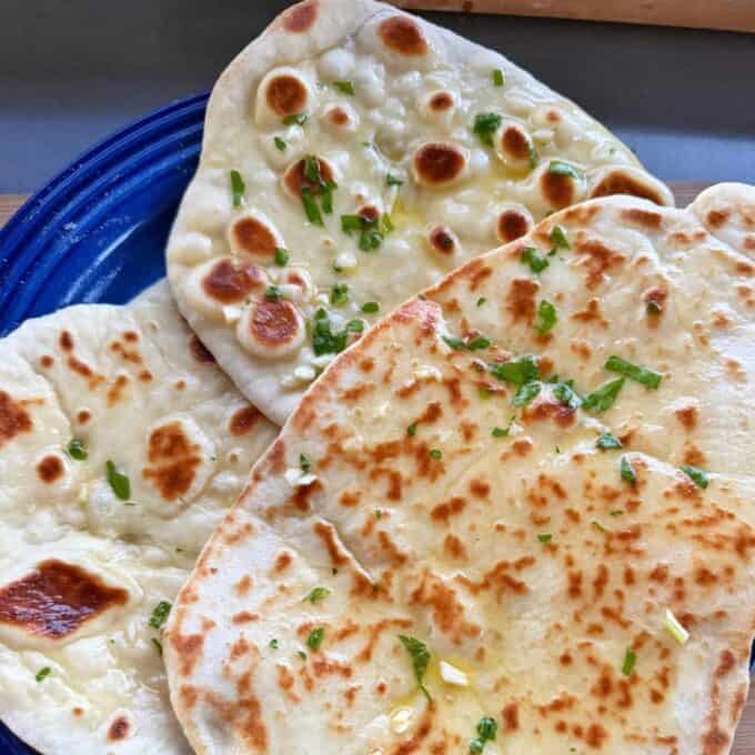 Homemade Garlic Naan Three pieces of garlic naan bread topped with fresh herbs on a blue plate.