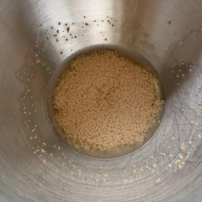 Homemade Garlic Naan Dry yeast granules soaking in a small amount of liquid in a metal mixing bowl.