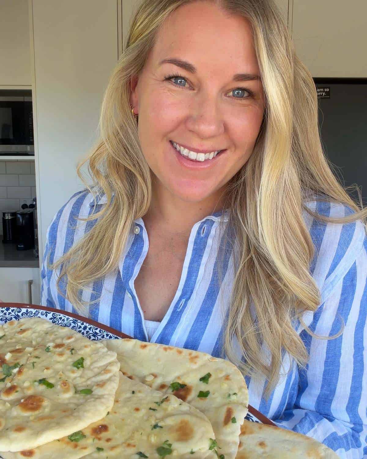 Homemade Garlic Naan A smiling woman in a blue and white striped shirt holding a platter of naan bread.
