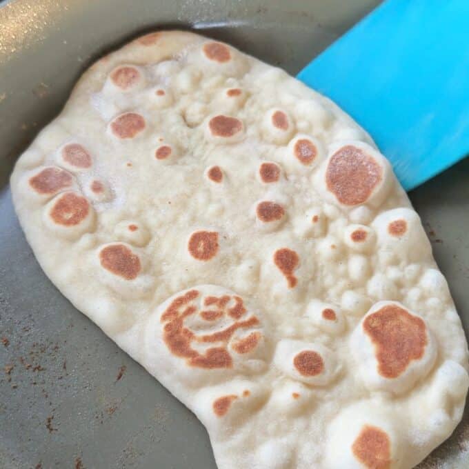 Homemade Garlic Naan Flatbread cooking in a pan with a blue spatula.