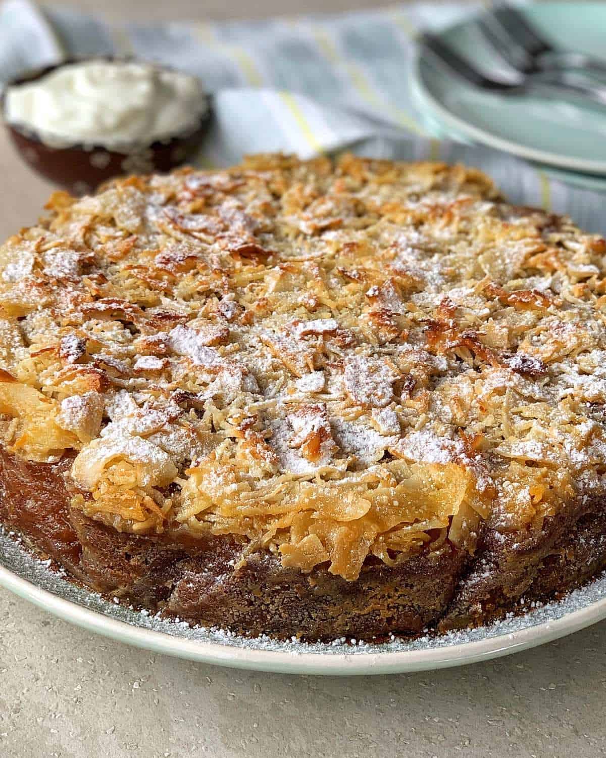 Lumberjack Cake A round cake topped with toasted coconut flakes and a dusting of powdered sugar on a plate.