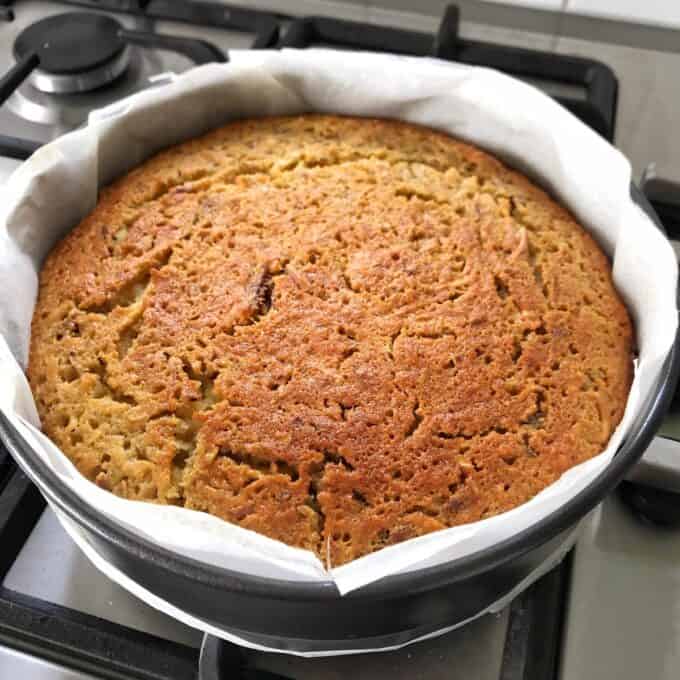 Lumberjack Cake A round, golden-brown baked cake in a springform pan lined with parchment paper, sitting on a stovetop.