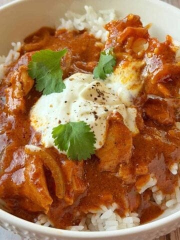 A bowl of chicken curry over white rice, topped with a dollop of sour cream and cilantro, with a forkful being lifted from the bowl.