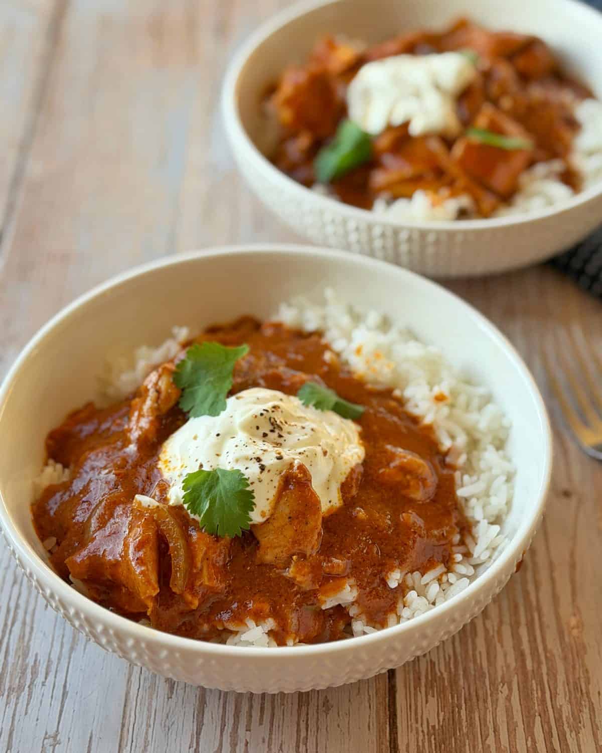 Slow Cooker Butter Chicken Two bowls of chicken curry served over white rice, topped with a dollop of cream and cilantro.
