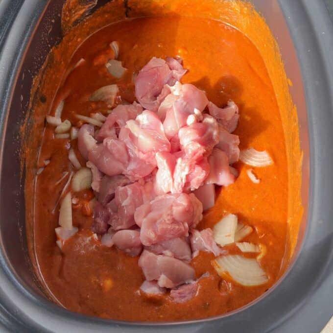 Slow Cooker Butter Chicken Raw chicken pieces and chopped onions in a slow cooker filled with orange sauce.