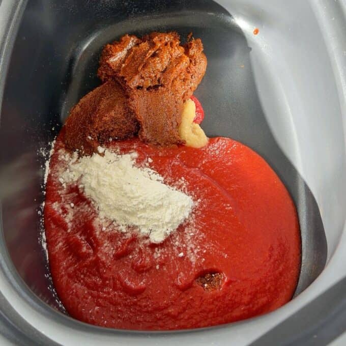 Slow Cooker Butter Chicken A slow cooker containing tomato sauce, a dollop of reddish-brown spice paste, and a pile of white powder.