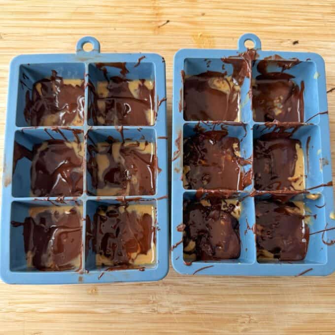 Snickers Peanut Butter Bites Two blue silicone ice cube trays filled with swirled melted chocolate and peanut butter.
