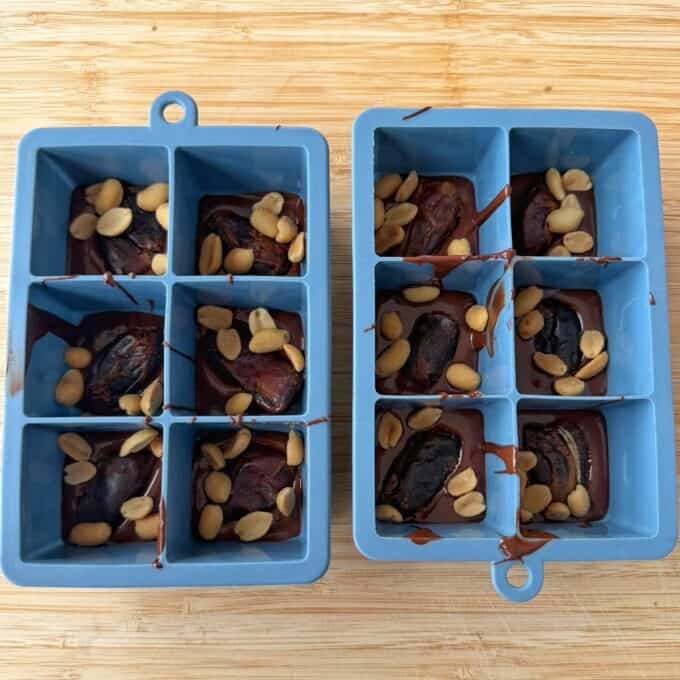 Snickers Peanut Butter Bites Two blue silicone ice cube trays filled with dates, peanuts, and melted chocolate.