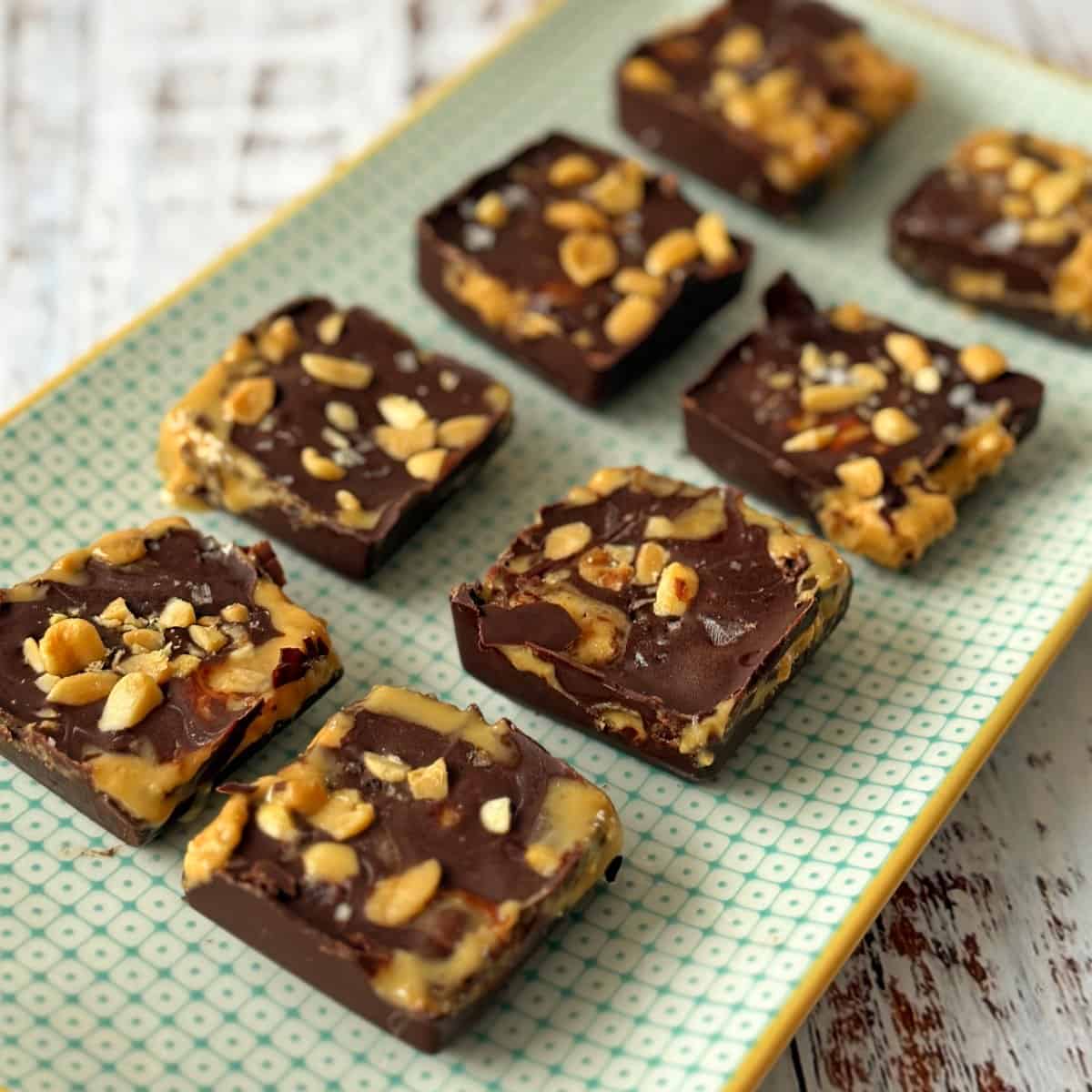 Snickers Peanut Butter Bites Eight square pieces of chocolate topped with peanuts and salt on a patterned rectangular tray.