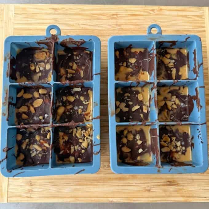 Snickers Peanut Butter Bites Two blue silicone molds filled with chocolate and peanut butter squares topped with chopped peanuts and salt.